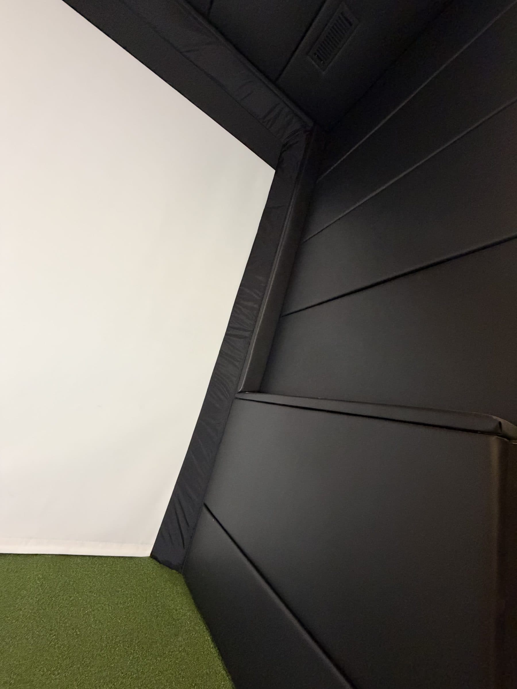 Matte black vinyl wall padding meeting the impact screen in a finished golf simulator bay
