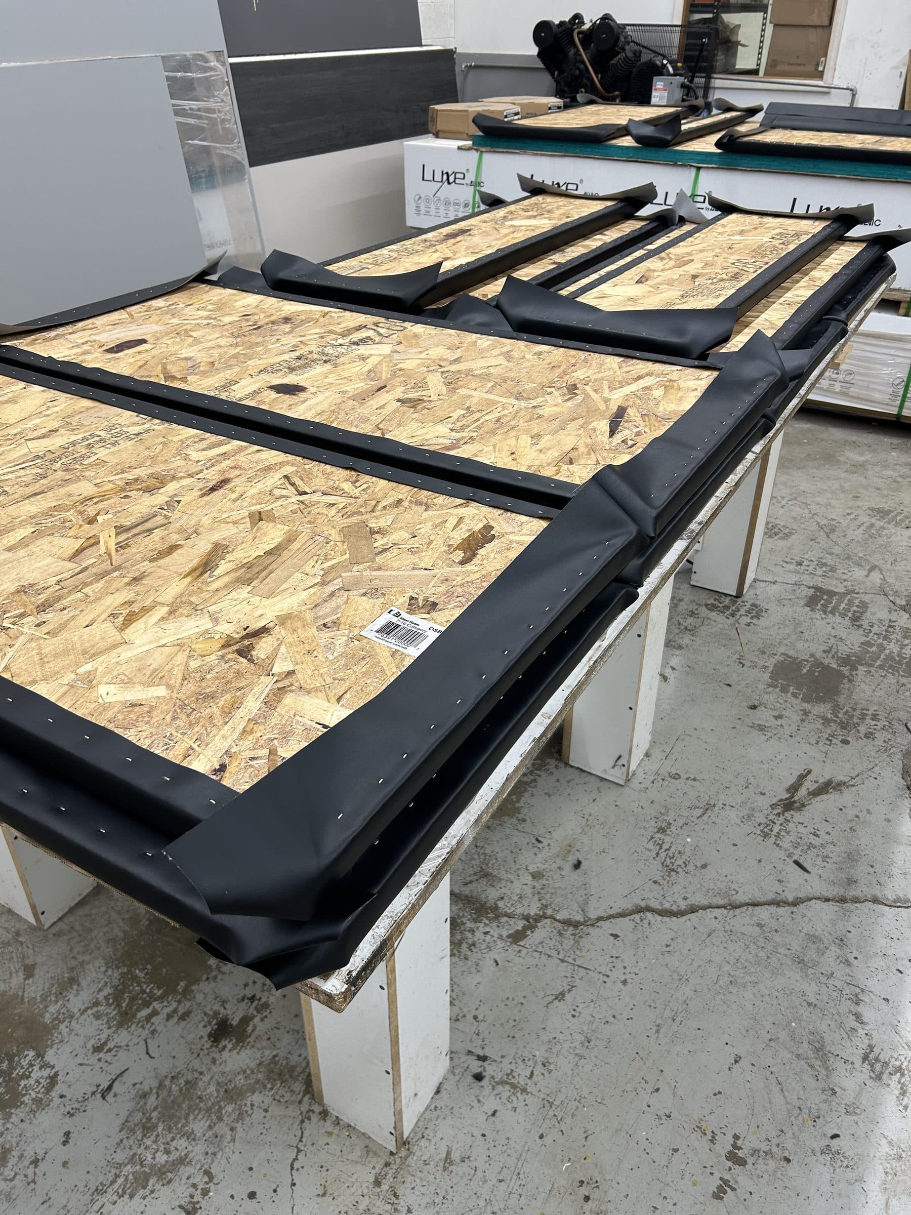Golf simulator wall panels laid face-down, showing the solid OSB backing beneath the wrapped vinyl edges